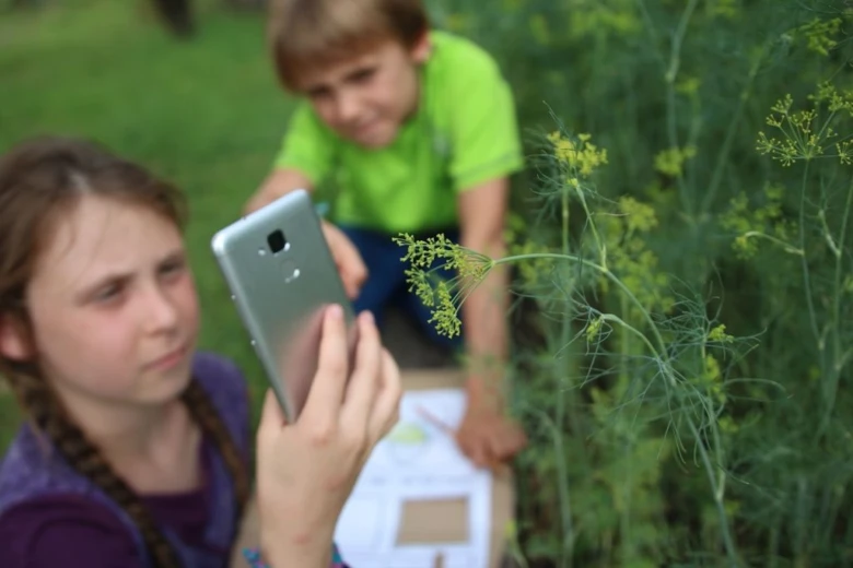 Dívka fotí rostlinu mobilním telefonem v zahradě.