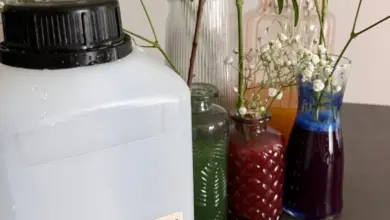 Bílá láhev s glycerinem mezi skleničkami se zelení a květinami.