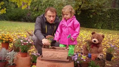 Muž s dívkou vysazují rostliny do květináče v zahradě.