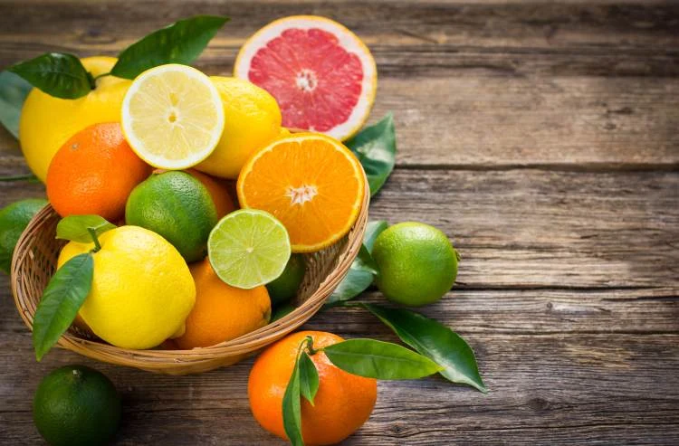 Košík s citrony, pomeranči, limetkami a plody calamondinu na dřevěném stole.