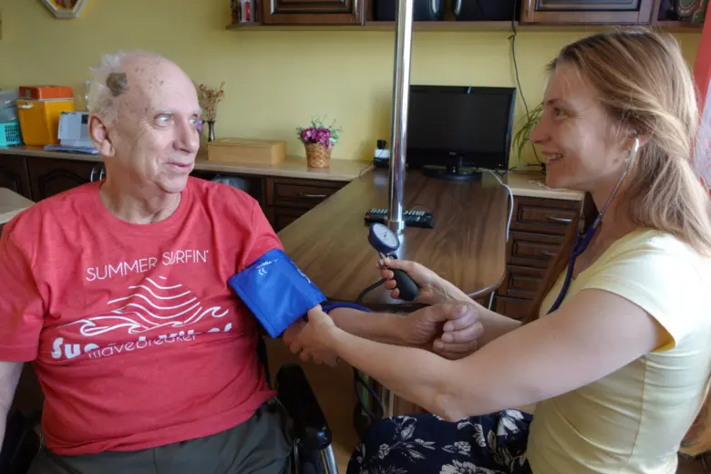 Pacientka měří krevní tlak seniorovi v jeho domácnosti.
