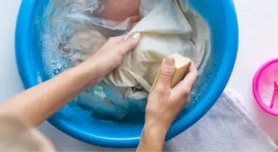 Ruční praní šatů v modré míse s mýdlem.