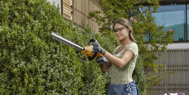 Žena prořezává živý plot elektrickým nůžkami v zahradě.