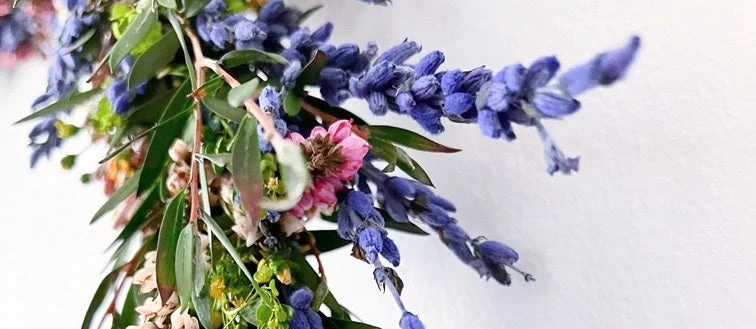 Suchá květinová aranžm s modrými růžemi a zelenou vegetací.