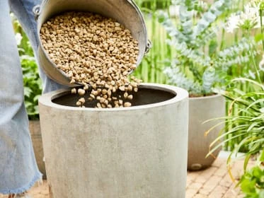 Lidá se z kbelíku do květináče granulovaný materiál pro odvodnění.