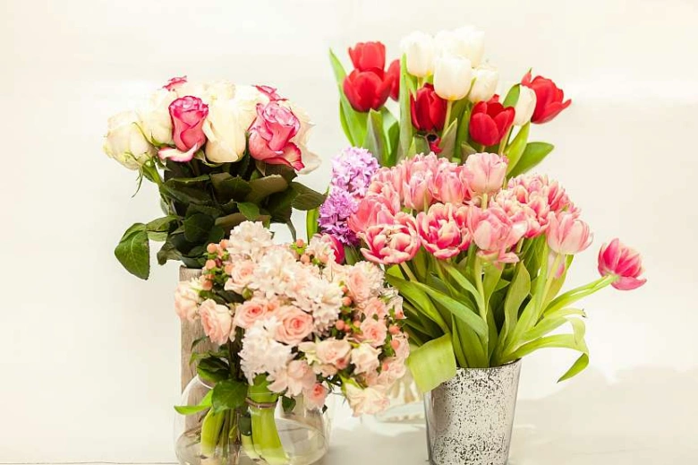 Svěží růže a tulipány ve vázách na bílém pozadí.