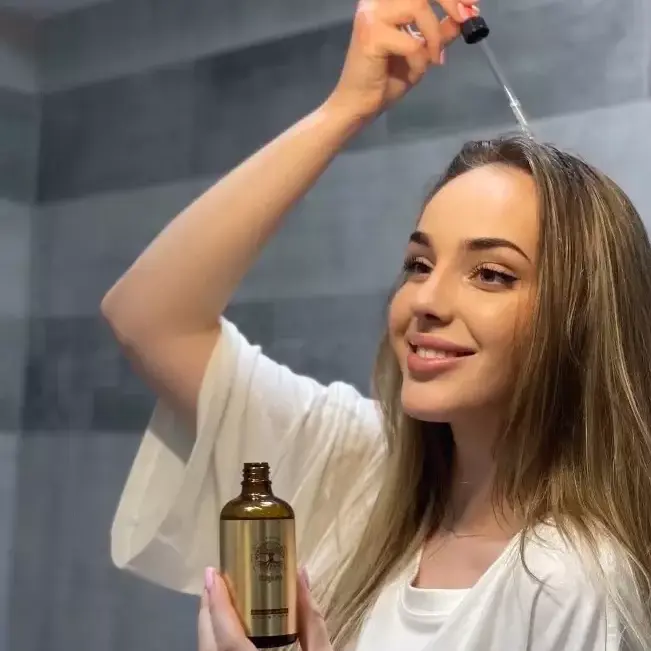 Žena aplikuje olej na vlasy z pipety v koupelně.