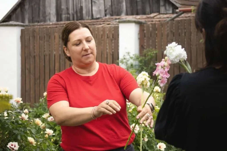 Žena v červené tričku upravuje květiny venku u růží.