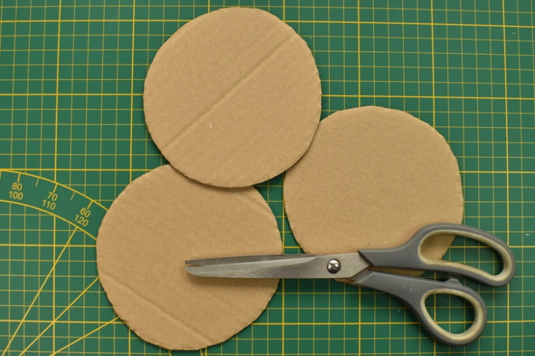 Tři kartonové kruhy na zeleném řezacím podkladu s nůžkami.